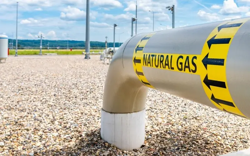 A close-up of a large-diameter high-pressure steel pipeline with a yellow 'NATURAL GAS' directional flow marker, installed on a concrete support at an onshore facility.-banner