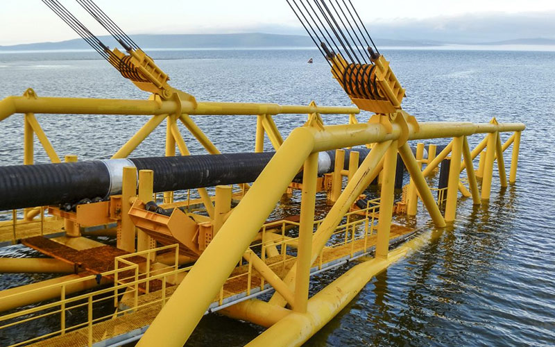 A large yellow pipe-laying vessel carefully lowering a black-coated API 5L X70 deep-sea pipeline into the water-banner