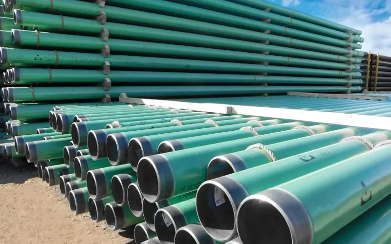 Large stacks of green, FBE-coated steel pipes with protected ends, ready for installation in an urban gas pipeline network.-banner