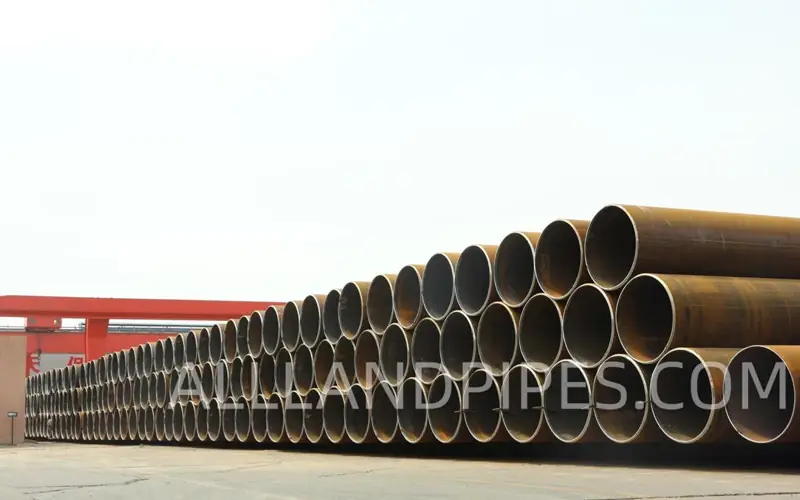 Large-diameter LSAW steel pipes neatly stacked in an outdoor storage yard before shipment. banner