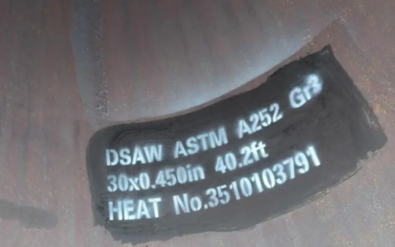 A close-up of a white stencil marking on the inner surface of a large-diameter DSAW steel pipe, showing the standard (ASTM A252 Gr3), size, and heat number for traceability-banner