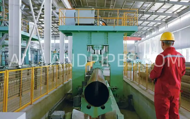 A technician supervising the manufacturing of a large-diameter LSAW pipe positioned inside a heavy-duty press in a factory.-banner