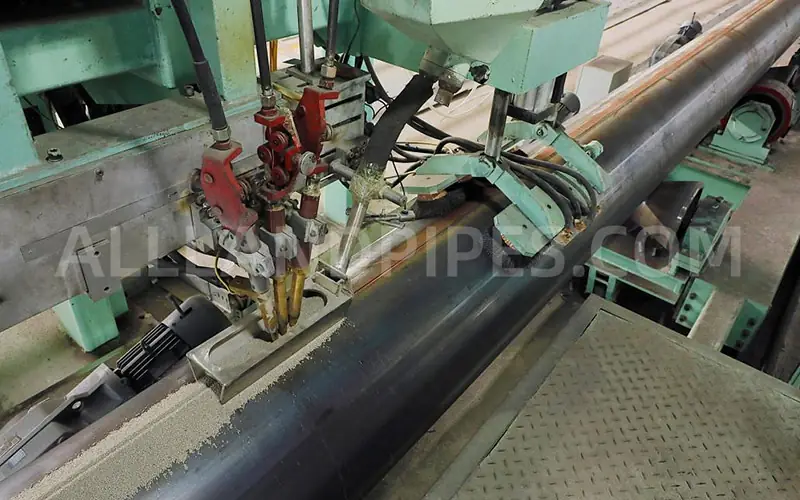 The SAW (Submerged Arc Welding) process in action, with granular flux covering the weld seam on a large steel pipe.-banner