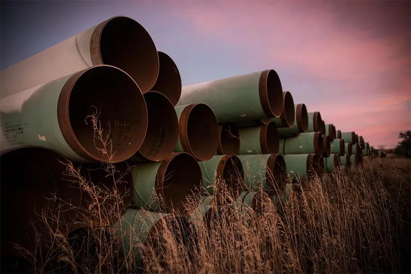 stacked large diameter api 5l pipes at sunset.