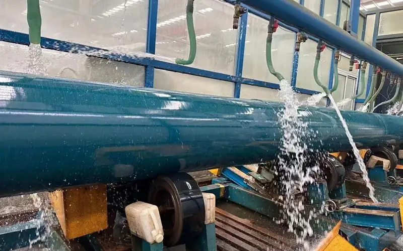 Steel pipe with fresh green FBE coating passing through water quench cooling tunnel at Allland factory. banner