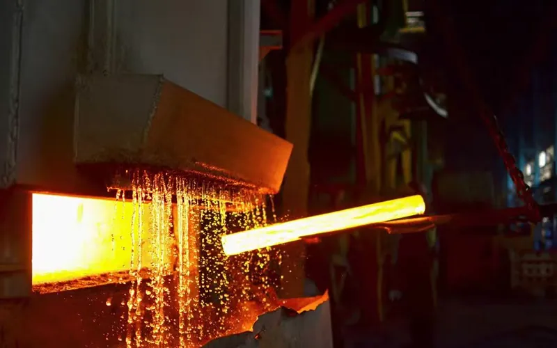Red-hot steel material emerging from a heat treatment furnace at 900°C - 950°C, demonstrating the mandatory normalizing process for API 5L PSL2 pipes.-banner