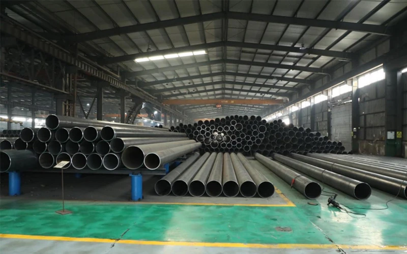 Stacked bundles of ERW steel pipes in a modern factory warehouse with a clear longitudinal weld seam profile - Allland Pipes banner
