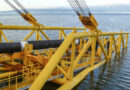 A large yellow pipe-laying vessel carefully lowering a black-coated API 5L X70 deep-sea pipeline into the water-banner
