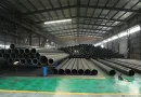 Stacked bundles of ERW steel pipes in a modern factory warehouse with a clear longitudinal weld seam profile - Allland Pipes banner