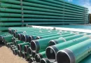 Large stacks of green, FBE-coated steel pipes with protected ends, ready for installation in an urban gas pipeline network.-banner