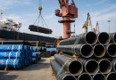 Large carbon steel pipes being loaded at an industrial port for overseas shipping from China, showcasing steel pipe export and logistics operations.