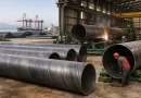Large diameter spiral steel pipes (SSAW) being welded and inspected in a China manufacturing factory with port logistics background-banner